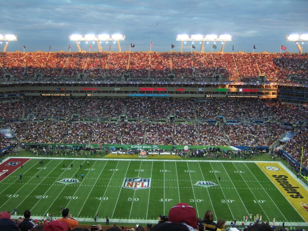 Um estádio de futebol americano lotado durante um jogo do Super Bowl, com as equipes alinhadas no campo e os torcedores enchendo as arquibancadas, no Raymond James Stadium em Westshore em Tampa.
