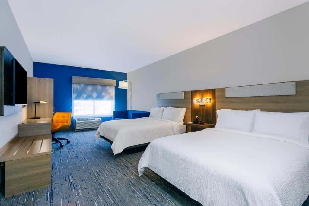 Quarto do Holiday Inn Express & Suites Tampa Stadium com duas camas de casal, uma escrivaninha com uma cadeira amarela, uma TV e uma janela com luz natural, para representar onde ficar em Tampa.