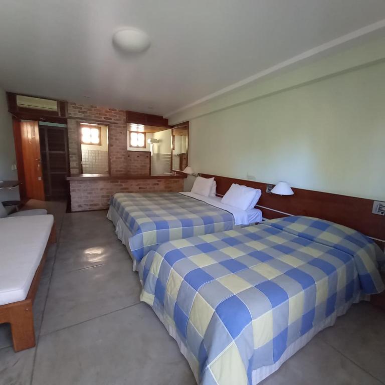 Quarto na Pousada Pilar com duas camas de casal, um banco, uma escrivaninha e uma área aberta mostrando o banheiro e a pia ao fundo, para representar pousadas em Arraial do Cabo.