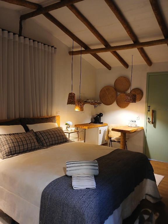 Quarto aconchegante com uma cama de casal, vigas de madeira, cestos de tecido na parede e uma pequena mesa com cafeteira, no Aconchego da Roça, para representar pousadas em Gonçalves.