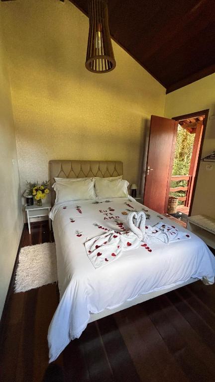 Uma cama bem arrumada com lençóis brancos, cisnes de toalha e pétalas de rosa em um quarto aconchegante com uma porta aberta para uma varanda, no Residencial das Araucárias, para representar pousadas em Gonçalves.