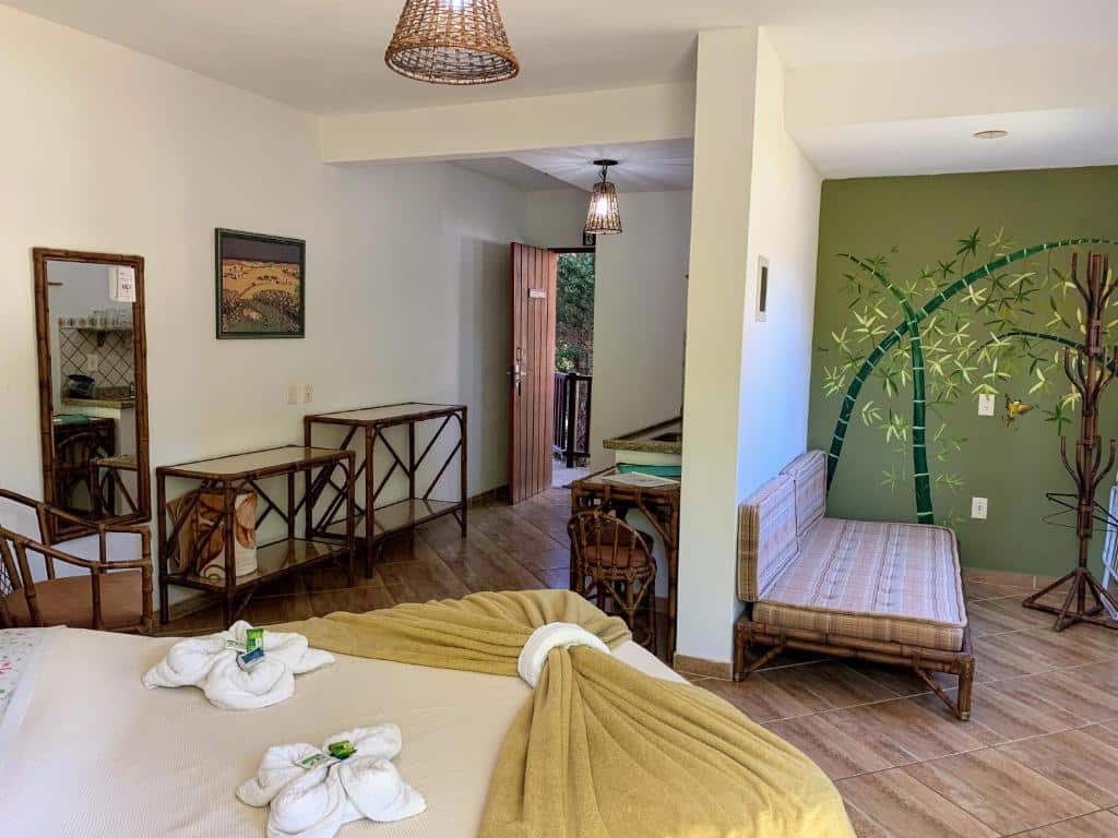 Um quarto no Riacho Das Pedras Pousada com uma cama, móveis de bambu, uma parede verde com um mural de árvore e toalhas dobradas sobre a cama, para representar pousadas em Gonçalves.