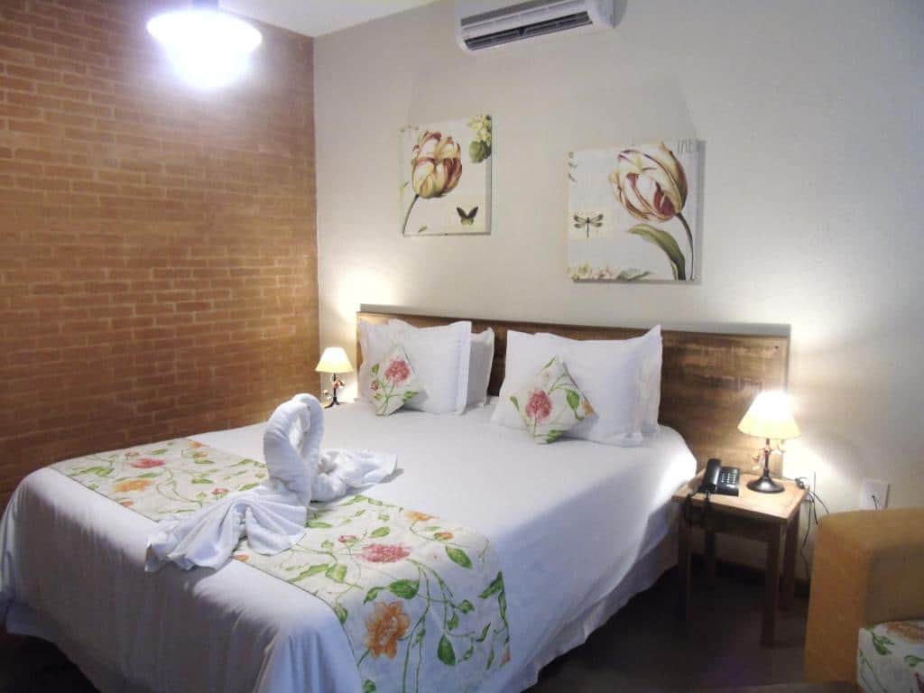 Um quarto na Pousada Villa dos Leais com uma cama de casal, decoração floral, abajures de cabeceira e uma toalha dobrada em forma de cisne sobre a cama, para representar pousadas em Serra Negra.