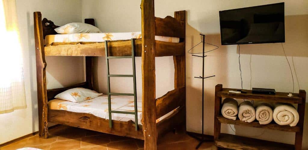 Quarto da Pousada Monte Verde com uma beliche feita de madeira rústica, uma cômoda com cobertas e uma televisão, para representar pousadas em Serra Negra.