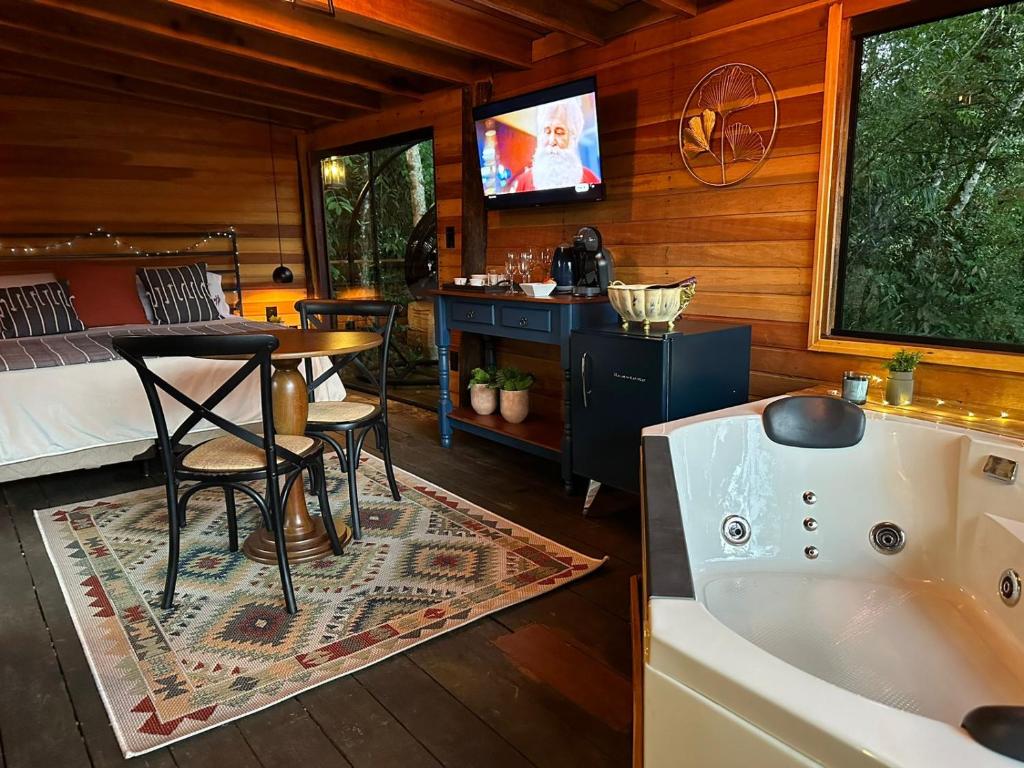 Interior aconchegante da cabine de madeira com uma cama, mesa redonda, poltronas, TV, tapete, cafeteira e uma banheira de hidromassagem ao lado da janela, na Pousada Santa Thereza, para representar pousadas em Serra Negra.