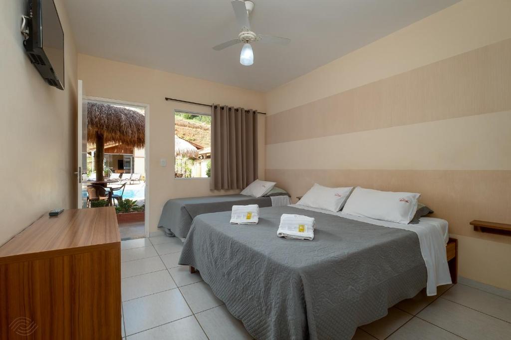 Foto do quarto da Pousada Pompeia, em Socorro, para representar o post sobre pousadas perto de Ribeirão Preto. Na suíte, há uma casa de casal e outra de solteiro em seu lado. Há uma janela e uma porta que da acesso para a área da piscina. No quarto também tem uma televisão na parede de frente para as camas.