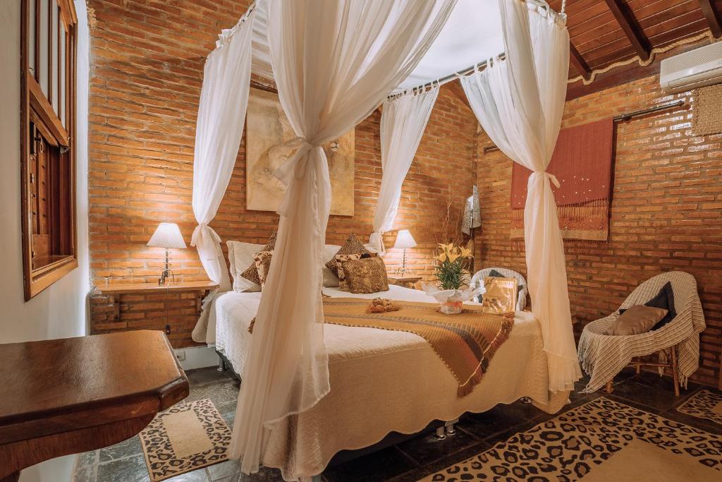 Imagem da Pousada das Nascentes, em Brotas, para ilustrar o post sobre pousadas perto de Ribeirão Preto. O quarto é bem iluminado, há um abajur dos dois lados da cama, que é de casal e bem aconchegante e possui cortinas. A suíte possui um ambiente romântico e confortável.