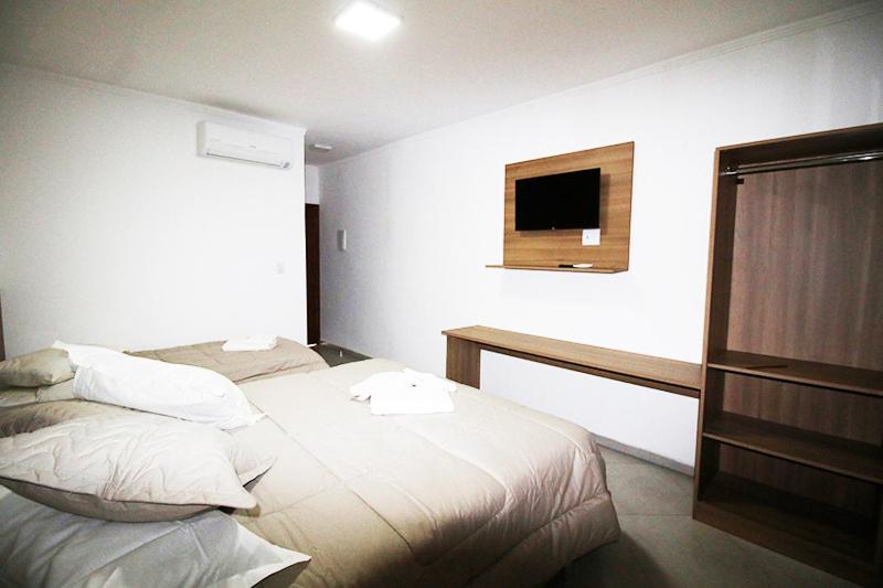 Quarto no Espaço Flório Hotel, em Araraquara, para ilustrar o post sobre pousadas perto de Ribeirão Preto. Na suíte, há uma cama de casal e outra de solteiro ao seu lado. Uma televisão fixa na parede está voltada de frente para as camas, e ao seu lado há um armário e uma mesa debaixo.