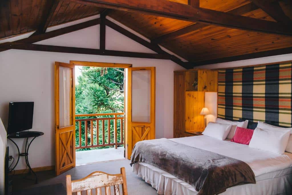 Quarto da Pousada Aberdeen. No lado direito há uma cama de casal e no lado esquerdo da cama há um armário e um abajur. No lado esquerdo há uma televisão em cima de uma pequena mesa redonda. Ao fundo há uma porta que dá acesso a varanda do quarto. Imagem utilizada para ilustrar o post pousadas pet friendly em Campos do Jordão.