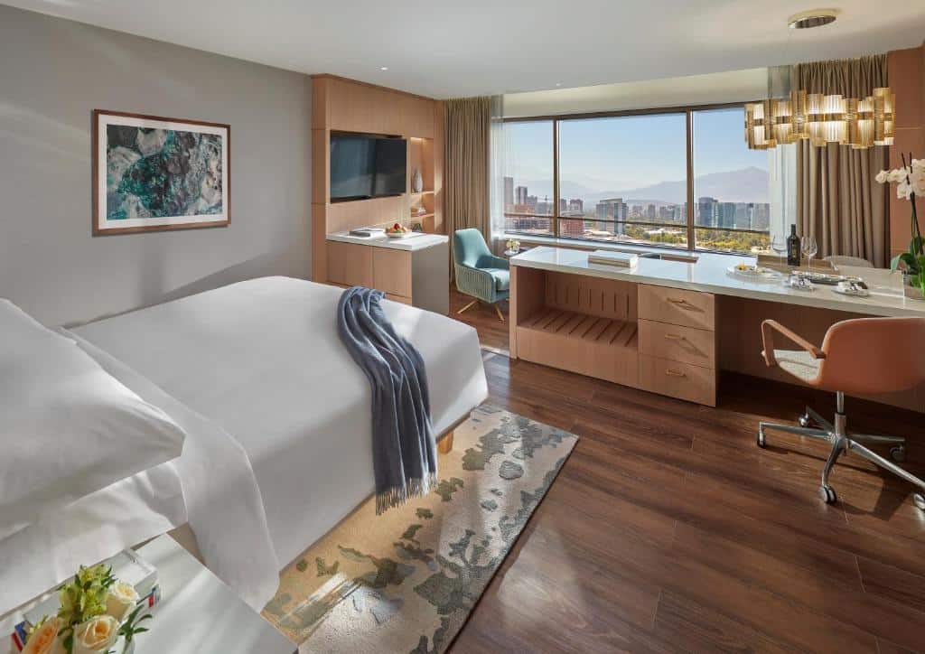 Quarto do Mandarin Oriental, Santiago com cama do lado esquerdo com mesa de trabalho do lado direito do quarto e a frente a cama uma pequena sala de estar com poltronas com janelas panorâmicas. 