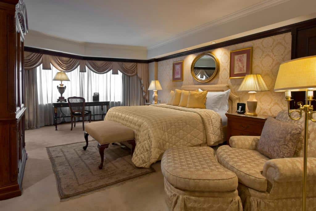 Quarto do Sheraton Santiago Hotel & Convention Center com poltrona do lado direito, ao lado uma cômoda de madeira com luminária, cama de casal no centro e do lado esquerdo mesa de trabalho.