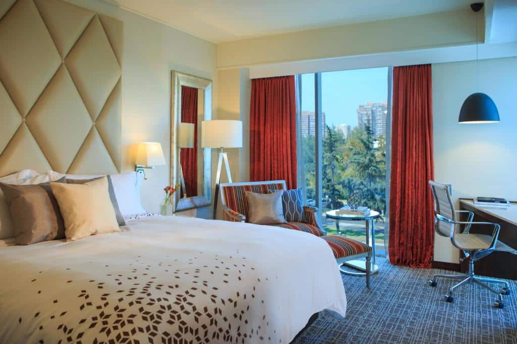 Quarto do Renaissance Santiago Hotel  com cama de casal do lado esquerdo, uma poltrona do lado esquerdo do quarto e logo a frente uma mesa de trabalho.