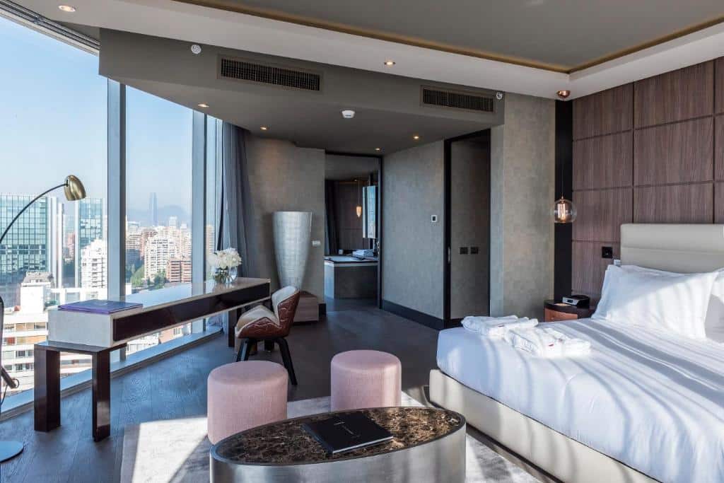 Quarto do Icon Hotel com cama de casal do lado direito e do lado esquerdo mesa de trabalho em frente a janelas panorâmicas. 