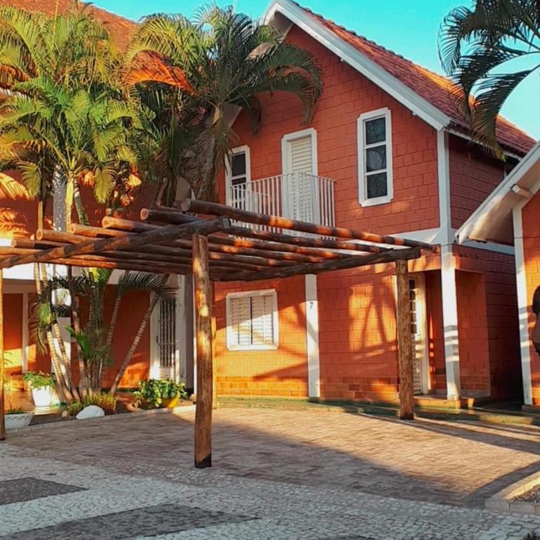 Uma casa de tijolos vermelhos de dois andares com telhado de telha, pérgola de madeira, palmeiras e entrada de automóveis pavimentada à luz do sol. Este é um dos Chalés Apart Hotel em Bonito. 