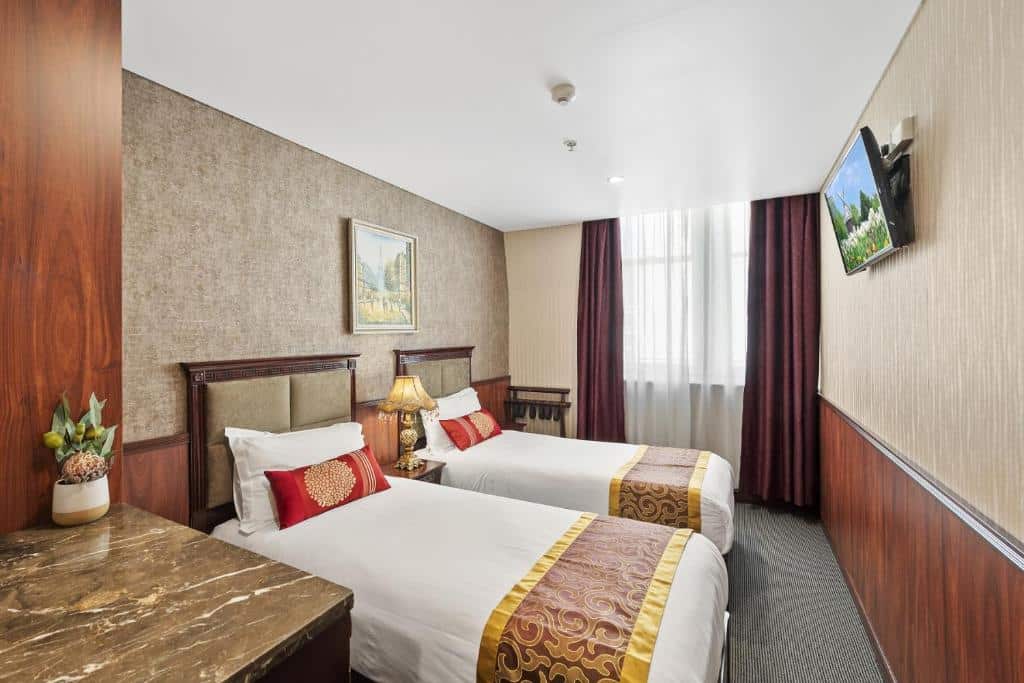 Quarto do YEHS Hotel Sydney CBD. Do lado direito uma TV, do lado esquerdo duas camas de solteiro, entre elas um abajur. No fundo uma janela com cortina.