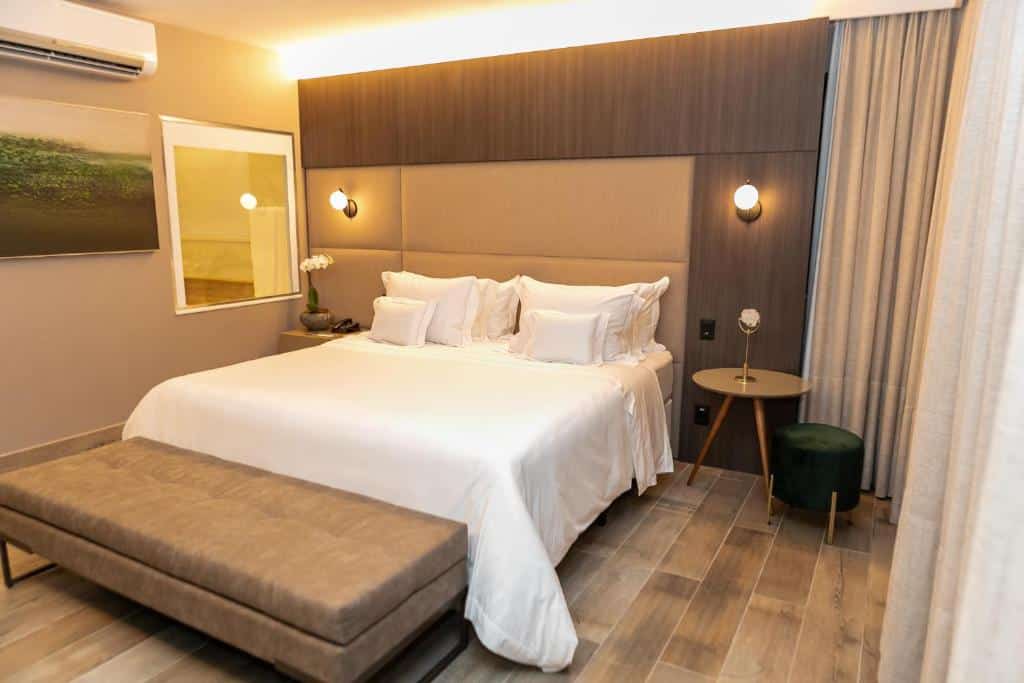 Quarto do Radisson Blu Belo Horizonte Savassi com cama de casal, com mesa ao lado direito e uma cômoda ao lado esquerdo com telefone em cima, na frente da cama há um banco estofado.