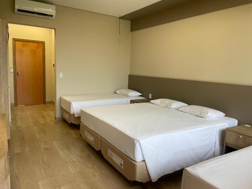 Quarto de hotel com três camas de solteiro, roupa de cama branca, piso de madeira, paredes bege e uma porta de madeira fechada.