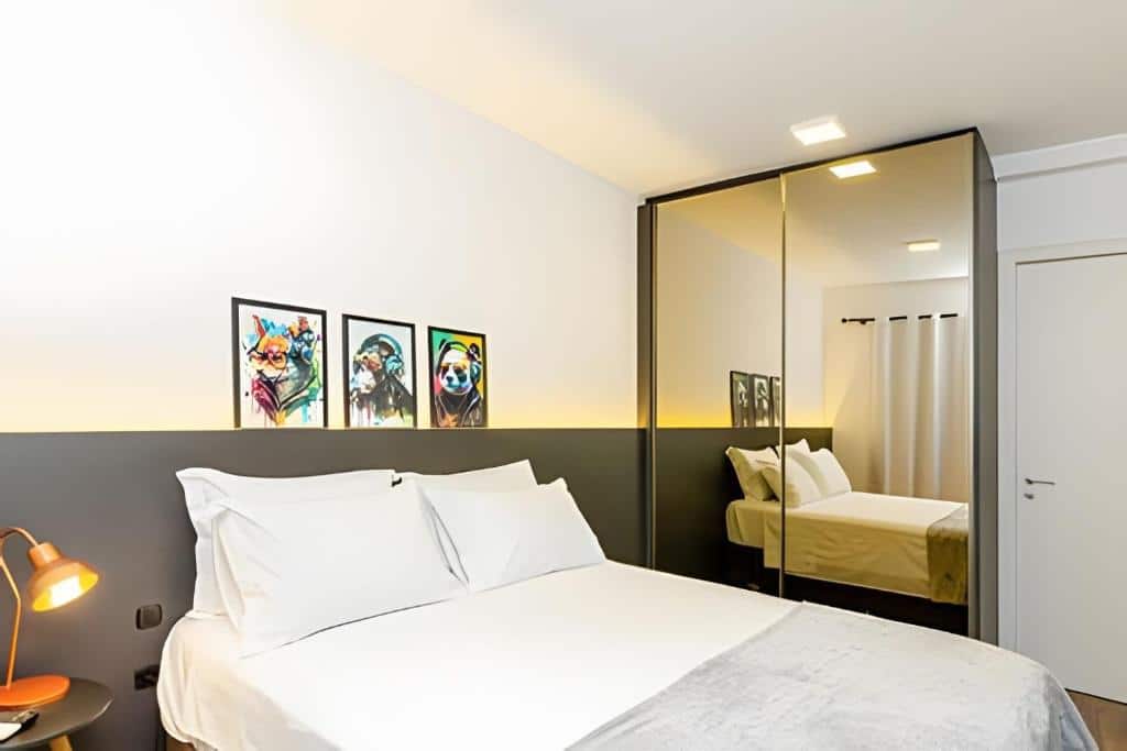 Quarto moderno com uma cama de casal, guarda-roupa espelhado, três gravuras de animais e iluminação aconchegante, no Sky Batel - Apartamento UROOMS, para representar airbnb em Curitiba.
