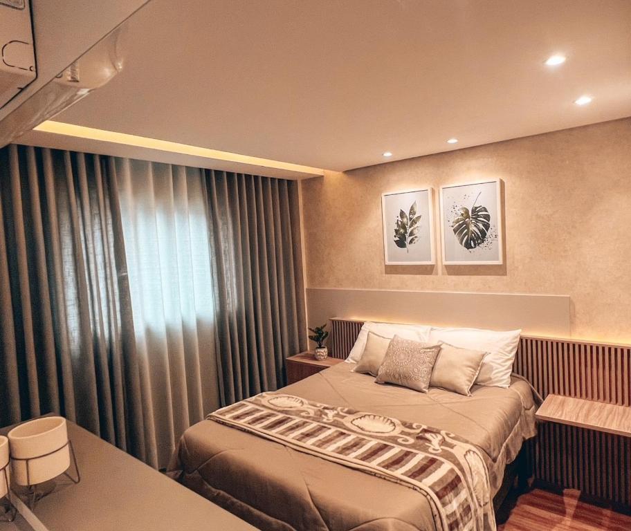Uma cama bem arrumada em um quarto moderno com decoração bege, mesas de cabeceira e obras de arte botânicas acima da cabeceira, no Apto conforto extremo, para representar airbnb em Curitiba.