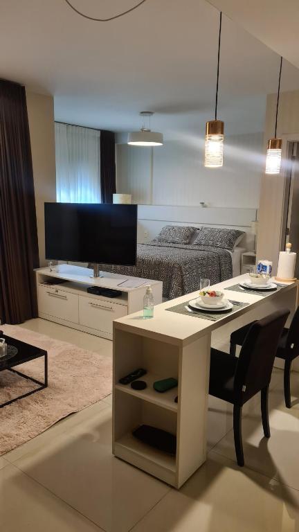Um apartamento estúdio moderno com cama, TV, mesa de centro, pequena área de jantar e decoração em tons neutros, no Studio, para representar airbnb em Curitiba.