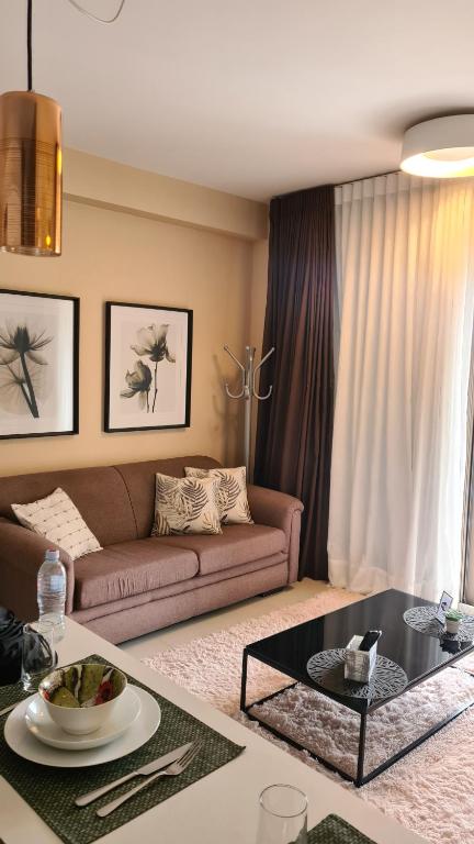 Uma sala de estar com um sofá marrom, duas gravuras florais emolduradas, uma mesa de centro e uma grande janela com cortinas, no Studio em Curitiba.