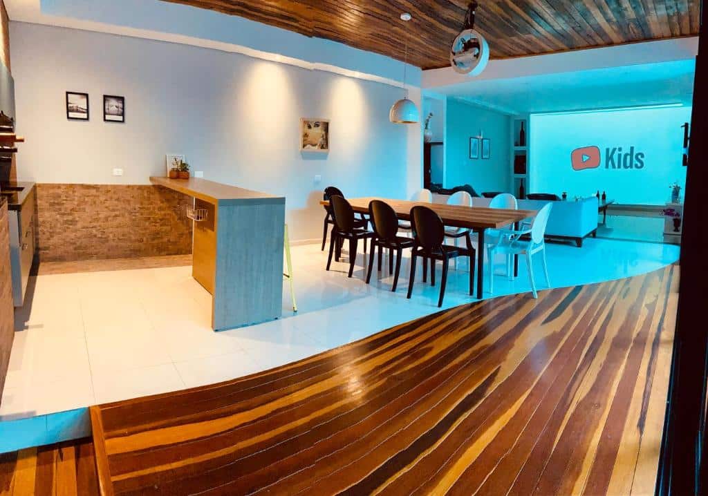 Moderna área de estar e jantar em plano aberto com piso de madeira e azulejo, uma mesa comprida e uma TV grande que exibe o YouTube Kids no CWB 997, em Curitiba.