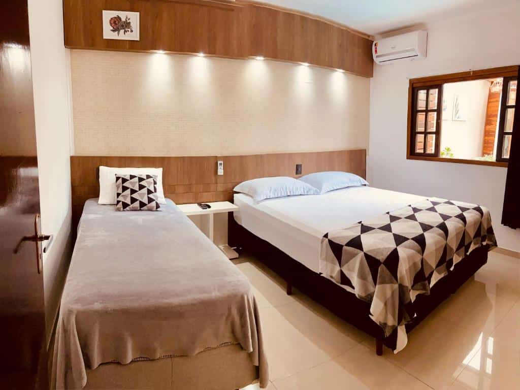 Um quarto com uma cama de solteiro e uma cama de casal, roupas de cama geométricas, uma mesa de cabeceira e uma janela com persianas abertas, no CWB 997 com piscina aquecida jacuzzi e Playground, para representar airbnb em Curitiba.