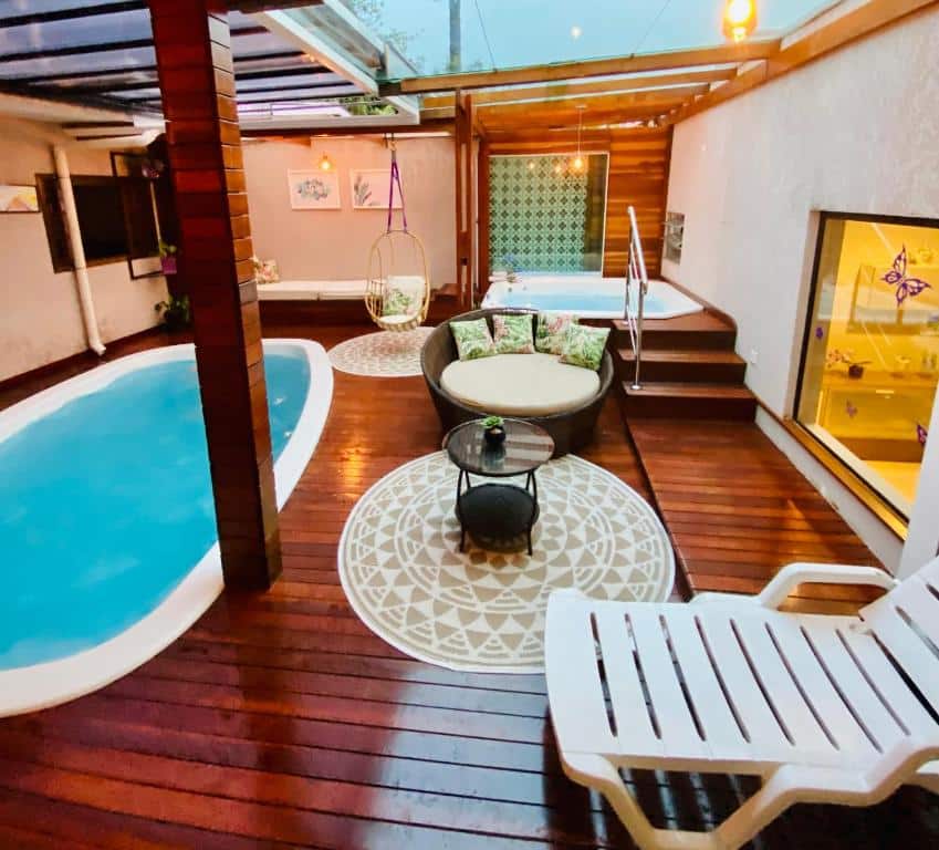 Um pátio coberto com uma pequena piscina, banheira de hidromassagem, espreguiçadeiras e um sofá redondo em um deck de madeira com tapetes decorativos, no CWB 997 com piscina aquecida jacuzzi e Playground.