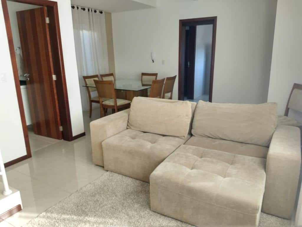 Um sofá seccional bege fica em uma sala de estar perto de uma mesa de jantar com quatro cadeiras, ao lado de uma porta e de um corredor, na Casa Curitiba 120m² (1 Suíte e 2 Quartos), para representar airbnb em Curitiba.
