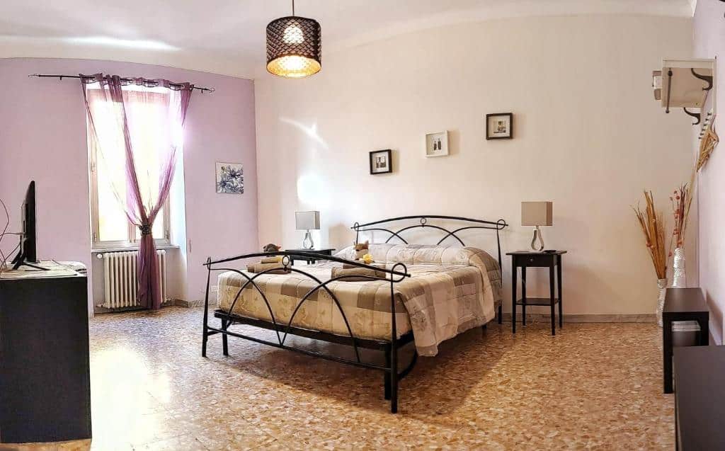 quarto do Holiday home Zia Gina, um airbnb em Roma, com cama de casal em decoração rústica, com mesinha e luminária de ambos os lados da cabeceira, com luz no teto, tv à frente, de um lado uma estante e, do outro, janela comprida com cortinas