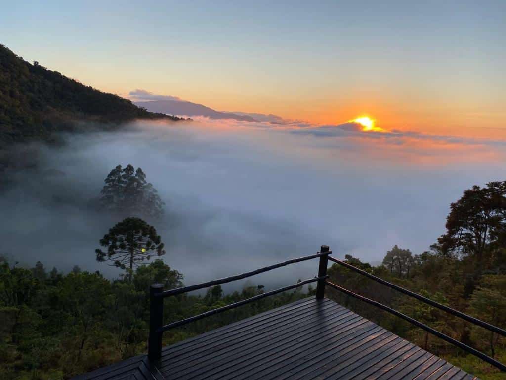 Vista de SFX de um chalé. Está nublado, o sol está nascendo. Vemos as montanhas e araucárias em São Francisco Xavier.