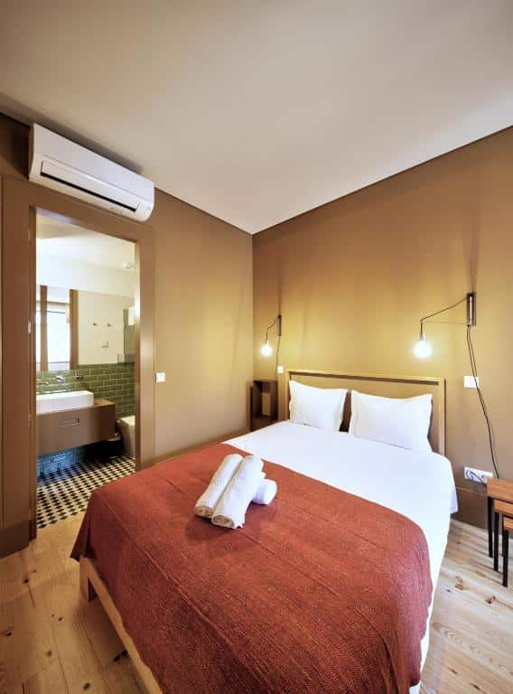 Quarto do Aparthotel Oporto Batalha com cama de casal do lado direito da imagem e do lado esquerdo porta que dá acesso ao banheiro. Representa airbnb no Porto.