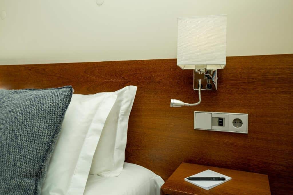 Quarto do Flores Lofts com cama de casal do lado esquerdo e do lado direito uma luminária com uma cômoda. 