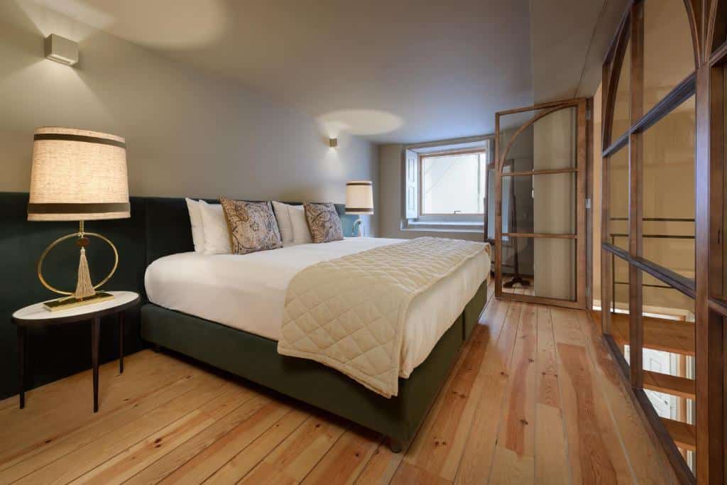 Quarto do Condes de Azevedo Palace Apartments com cama de casal do lado esquerdo da imagem e do lado esquerdo da cama uma cômoda com luminária. Representa airbnb no Porto.