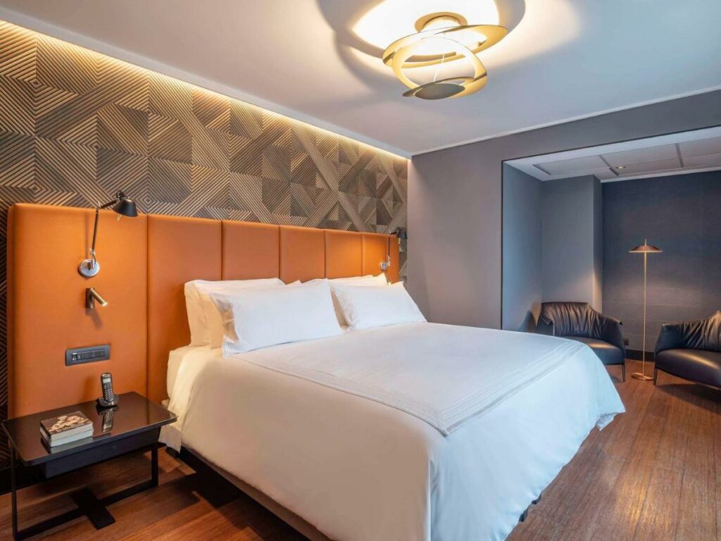 Quarto do Pullman Santiago Vitacura com cama de casal do lado esquerdo da imagem com uma cômoda do lado direito da imagem do lado esquerdo da cama duas poltronas. Representa hotéis 5 estrelas em Santiago.