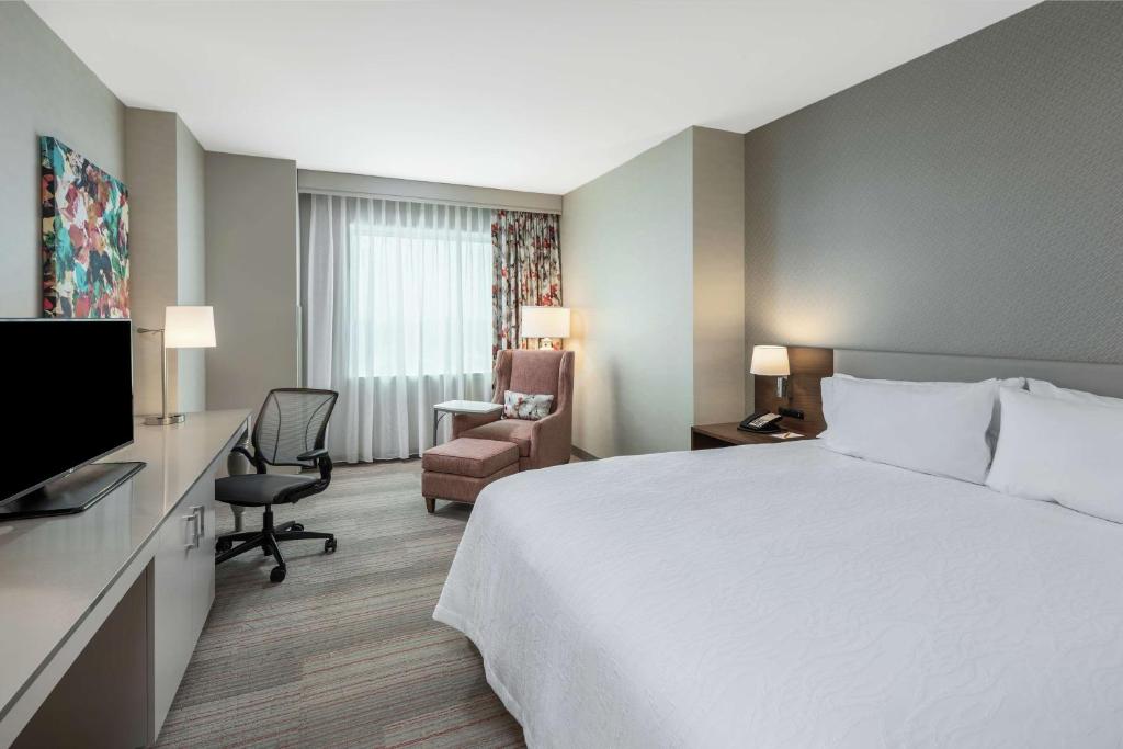 Quarto do Hilton Garden Inn Miami Dolphin Mall com cama de casal do lado direito da imagem do lado direito da cama uma cômoda com luminária e telefone em frente a cama uma cômoda com TV em cima do lado direito da cama uma poltrona e uma cadeir, para representar hotéis baratos em Miami.