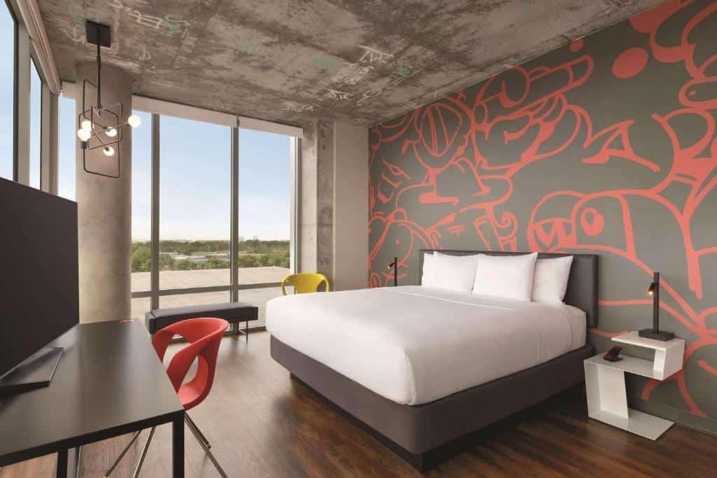 Quarto do Radisson RED Miami Airport com cama de casal do lado direito da imagem com uma comoda do lado esquerdo da cama em frente a cama uma mesa com cadeia e uma TV em cima, para representar hotéis baratos em Miami.