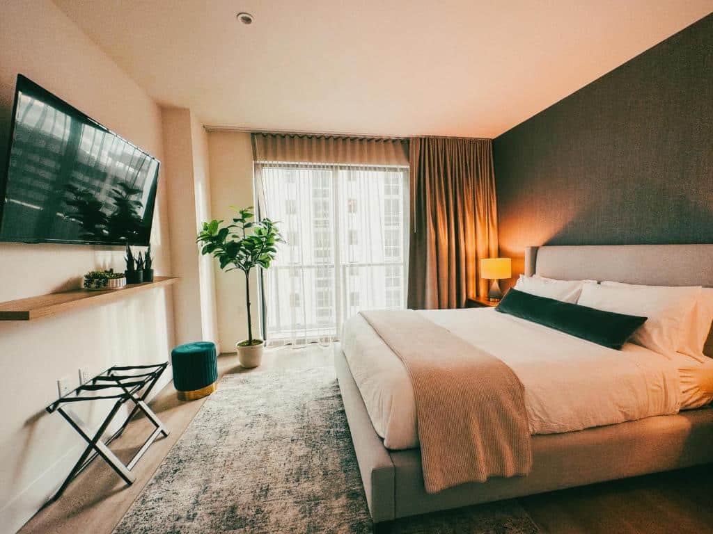 Quarto do Smart Brickell Hotel com cama de casal do lado direito da imagem do lado direito uma cômoda com luminária em frente a cama uma TV presa na parede, para representar hotéis baratos em Miami.
