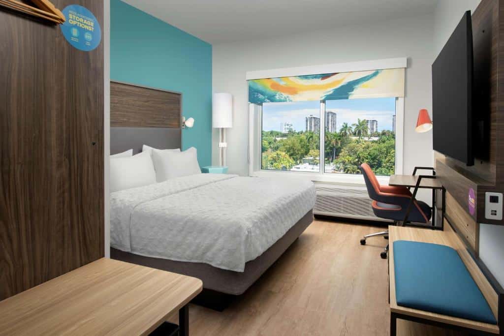 Quarto do Tru By Hilton Miami West Brickell com cama de casal do lado esquerdo da imagem em frente a cama uma mesa com cadeira do lado esquerdo no centro a TV presa na parede, para representar hotéis baratos em Miami.