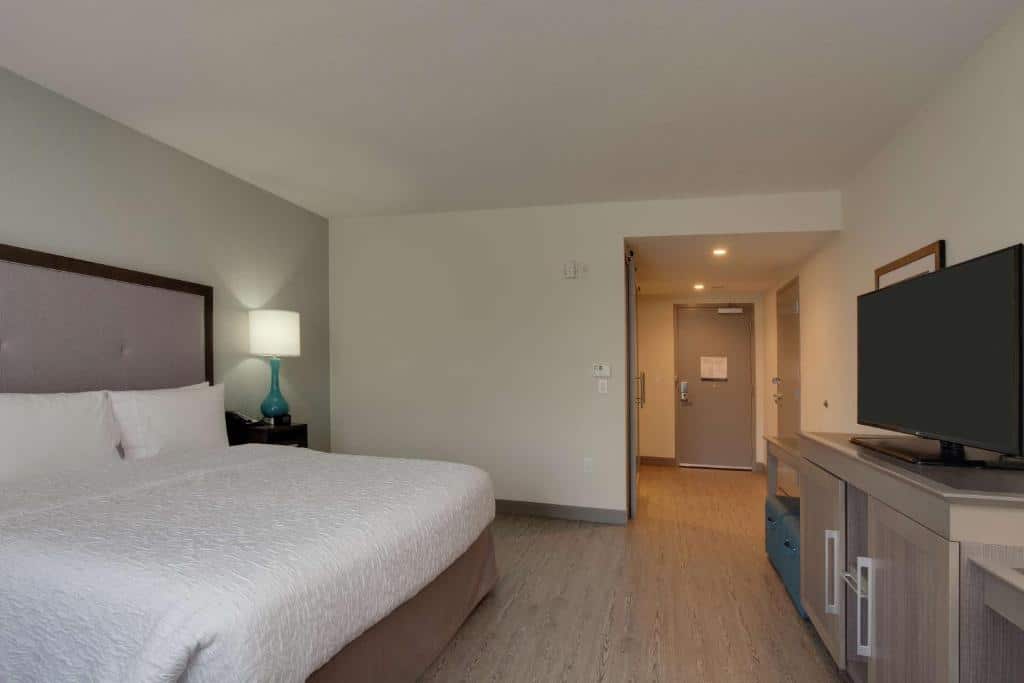 Quarto do Hampton Inn & Suites Miami Wynwood Design District, FL com cama de casal do lado esquerdo com uma cômoda com luminária do lado esquerdo da cama e em frente uma cômoda com TV em cima, para representar hotéis baratos em Miami.