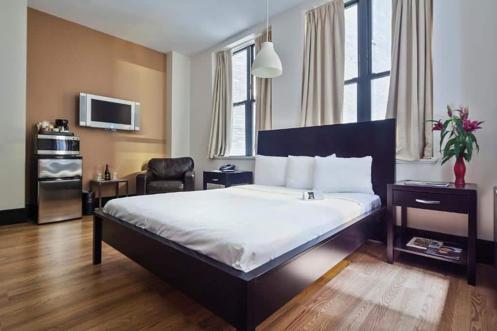 quarto do Eurostars Wall Street com cama de casal, mesinhas de cabeceira, poltrona, TV, frigobar, janelas e piso de madeira.