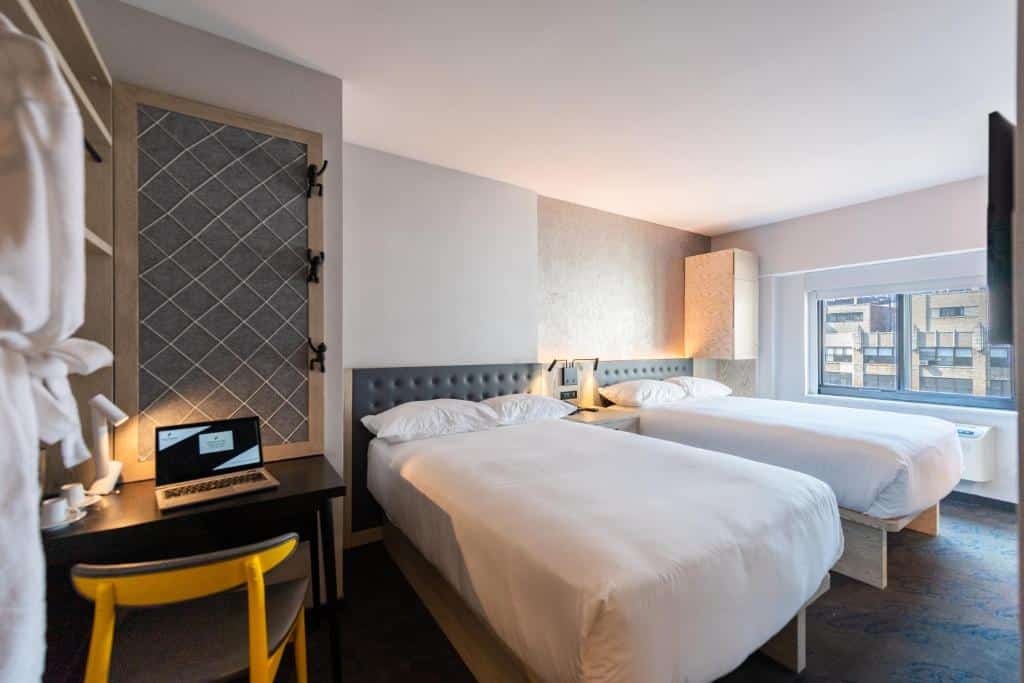 quarto do Pestana CR7 Times Square com duas camas de casal, uma escrivaninha com laptop e cadeira, uma janela e decoração moderna e neutra.