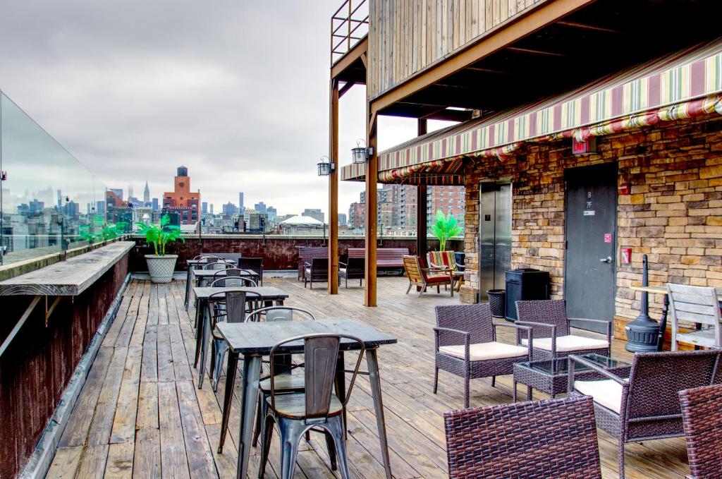 Deck na cobertura do The Ridge hotel com piso de madeira, mesas, cadeiras, assentos de vime e prédios da cidade visíveis ao fundo. Um dos hotéis baratos em Nova York.