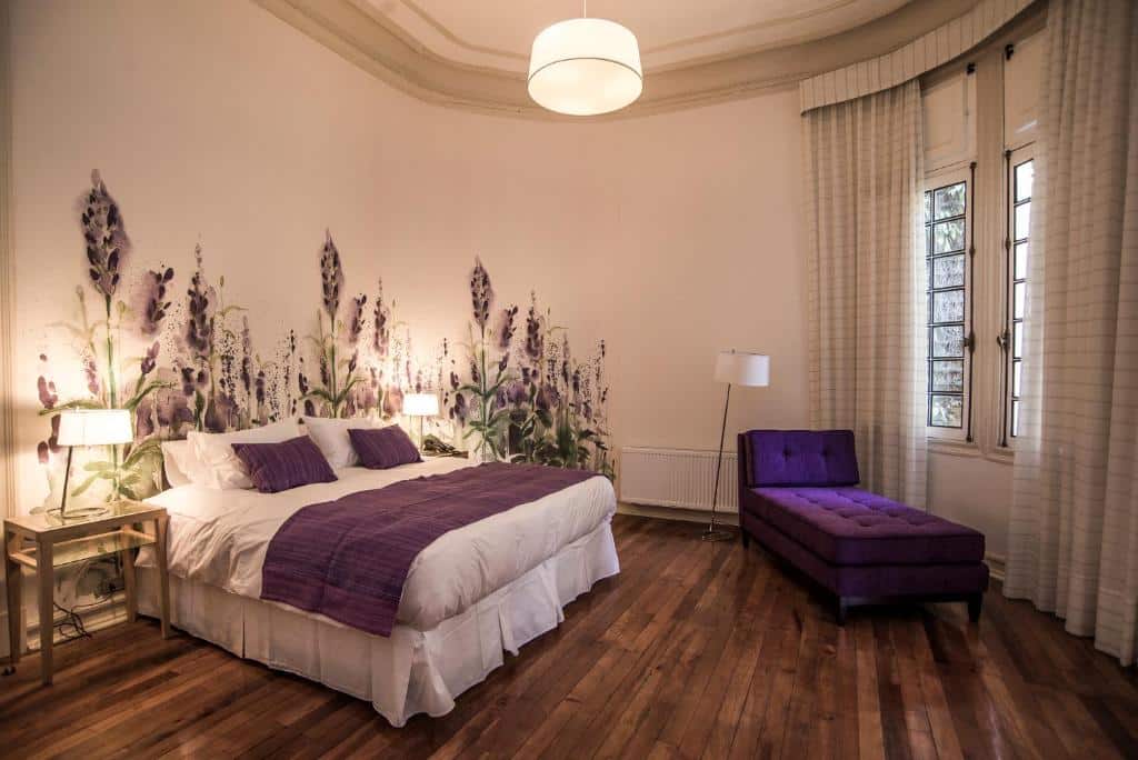 Quarto do Matildas Hotel Boutique com cama de casal do lado esquerdo e do lado esquerdo do quarto uma poltrona roxa. 