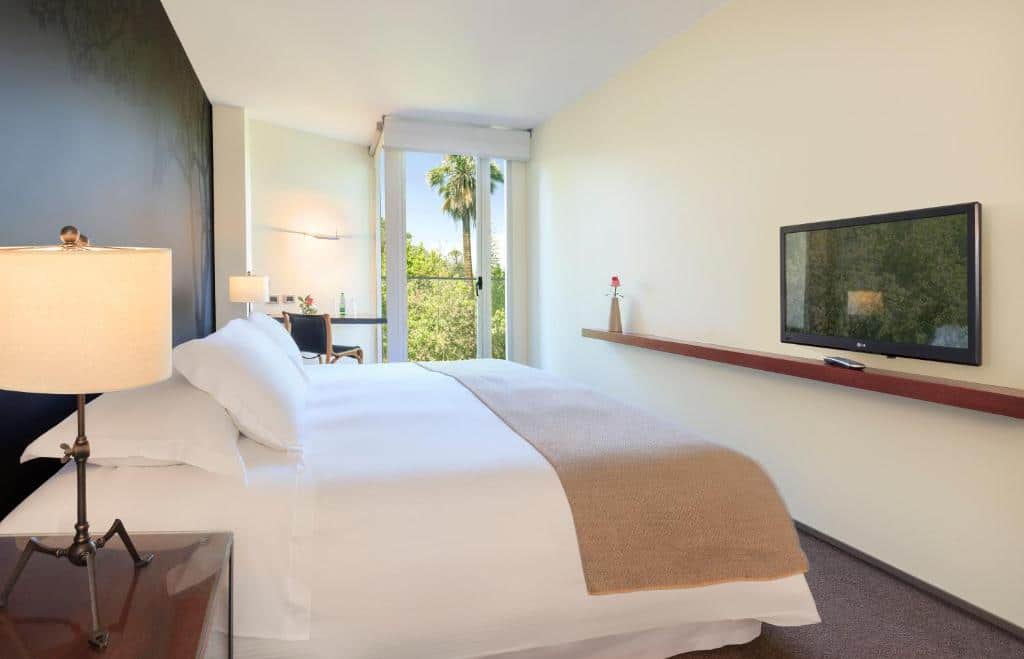 Quarto do Hotel Ismael com cama de casal no centro, duas cômodas ao lado da cama com luminária e em frente a cama com TV.