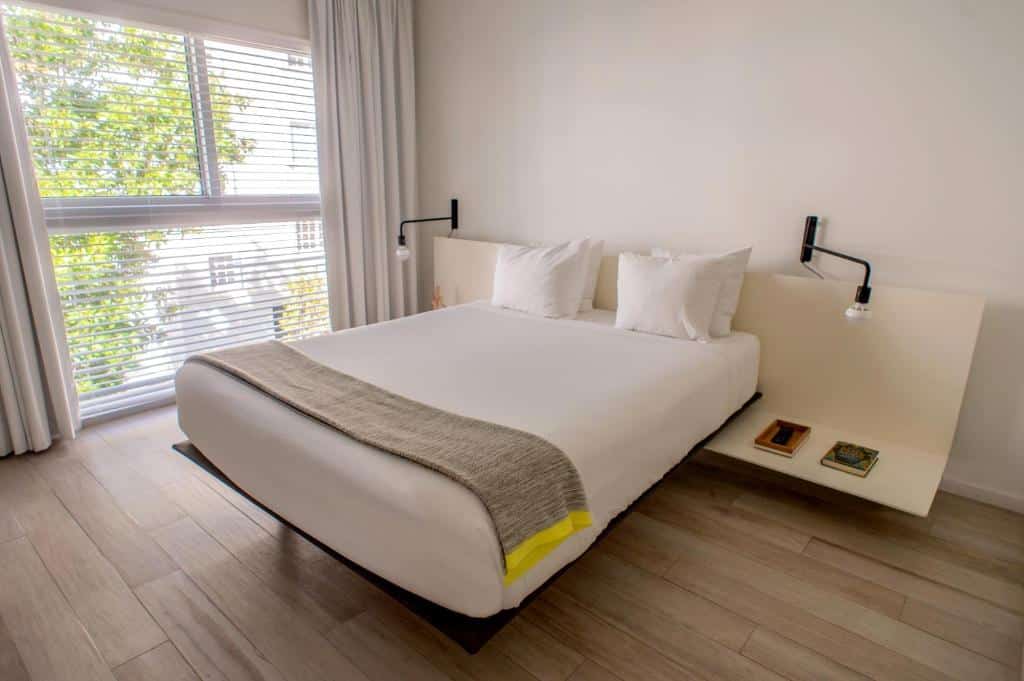 Quarto do Beach Haus Key Biscayne Contemporary Apartments com cama de casal, duas luminárias ao lado da cama preso na cabeceira da cama, do lado esquerdo janelas com cortinas brancas, para representar hotéis com cozinha em Miami.