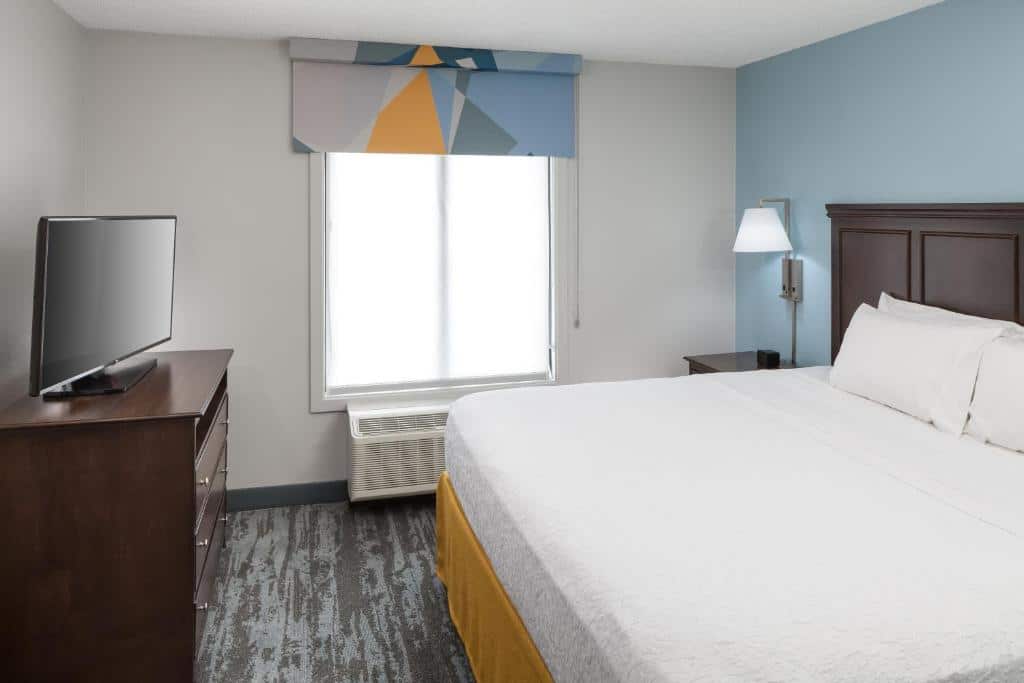 Quarto do Hampton Inn & Suites Miami-Doral Dolphin Mall  com cama de casal, cômoda do lado esquerdo, cômoda de madeira em frente a cama com TV, para representar hotéis com cozinha em Miami.