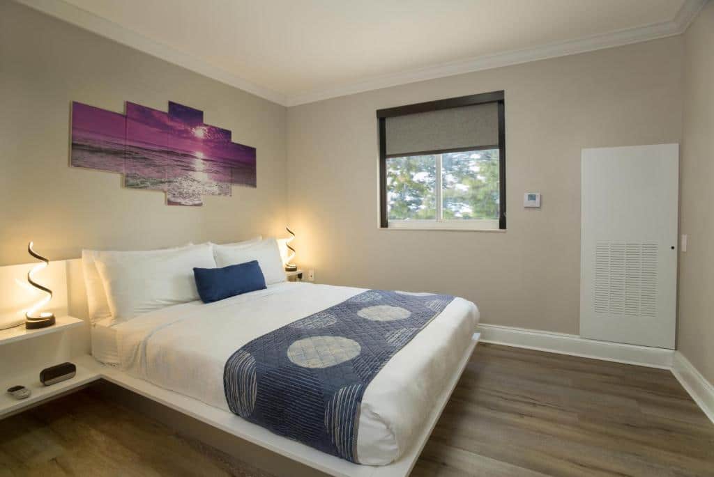 Quarto do Nuvo Suites Hotel – Miami / Doral com cama de casal, duas cômodas ao lado da cama com luminária, para representar hotéis com cozinha em Miami.