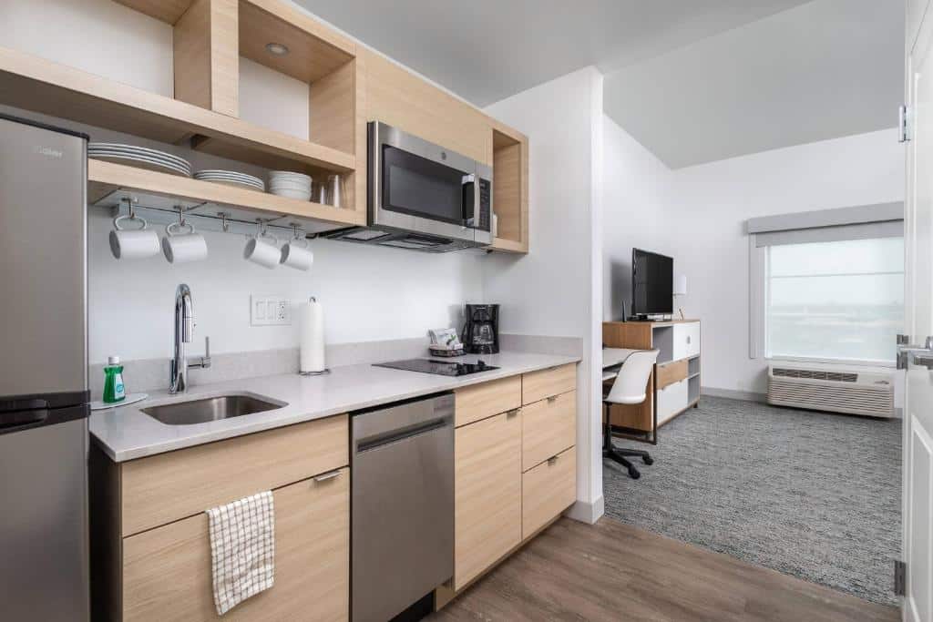 cozinha com forno, micro-ondas, pia e geladeira em tons de inox com armários de madeira clara e louça branca no TownePlace Suites By Marriott Orlando Southwest Near Universal, um dos hotéis com cozinha em Orlando