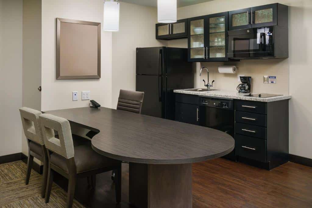 cozinha com mesa grande e cadeiras em tons cinza, com geladeira, fogão, forno e armários com pratos e talheres no Candlewood Suites - Orlando - Lake Buena Vista, an IHG Hotel, um dos hotéis com cozinha em Orlando